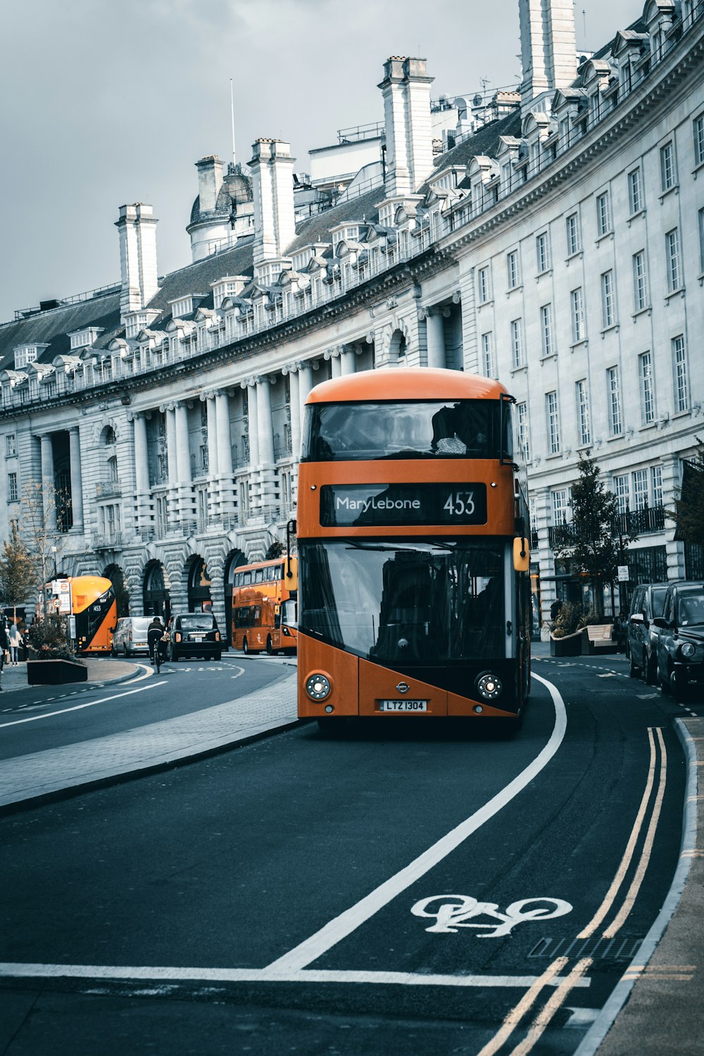 낮 동안 흰색 콘크리트 건물 근처 도로에서 주황색과 검은색 버스
