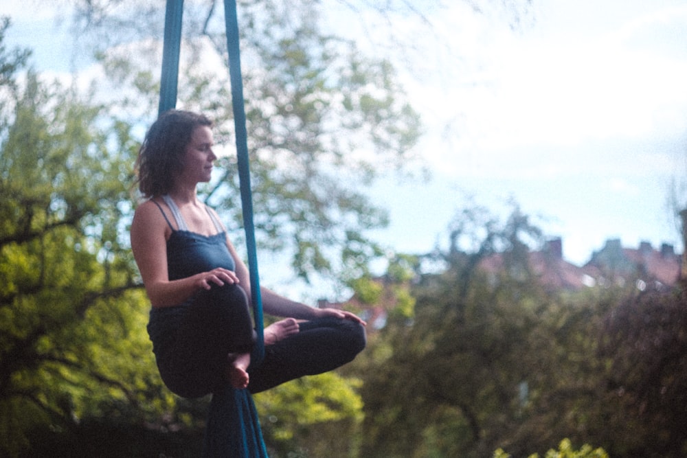 woman in black tank top and blue denim jeans sitting on blue hammock during daytime