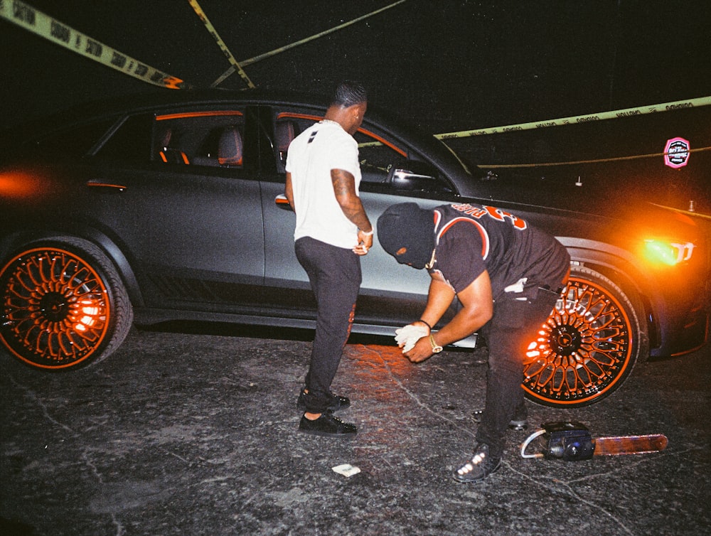 man in white t-shirt and black pants leaning on black car