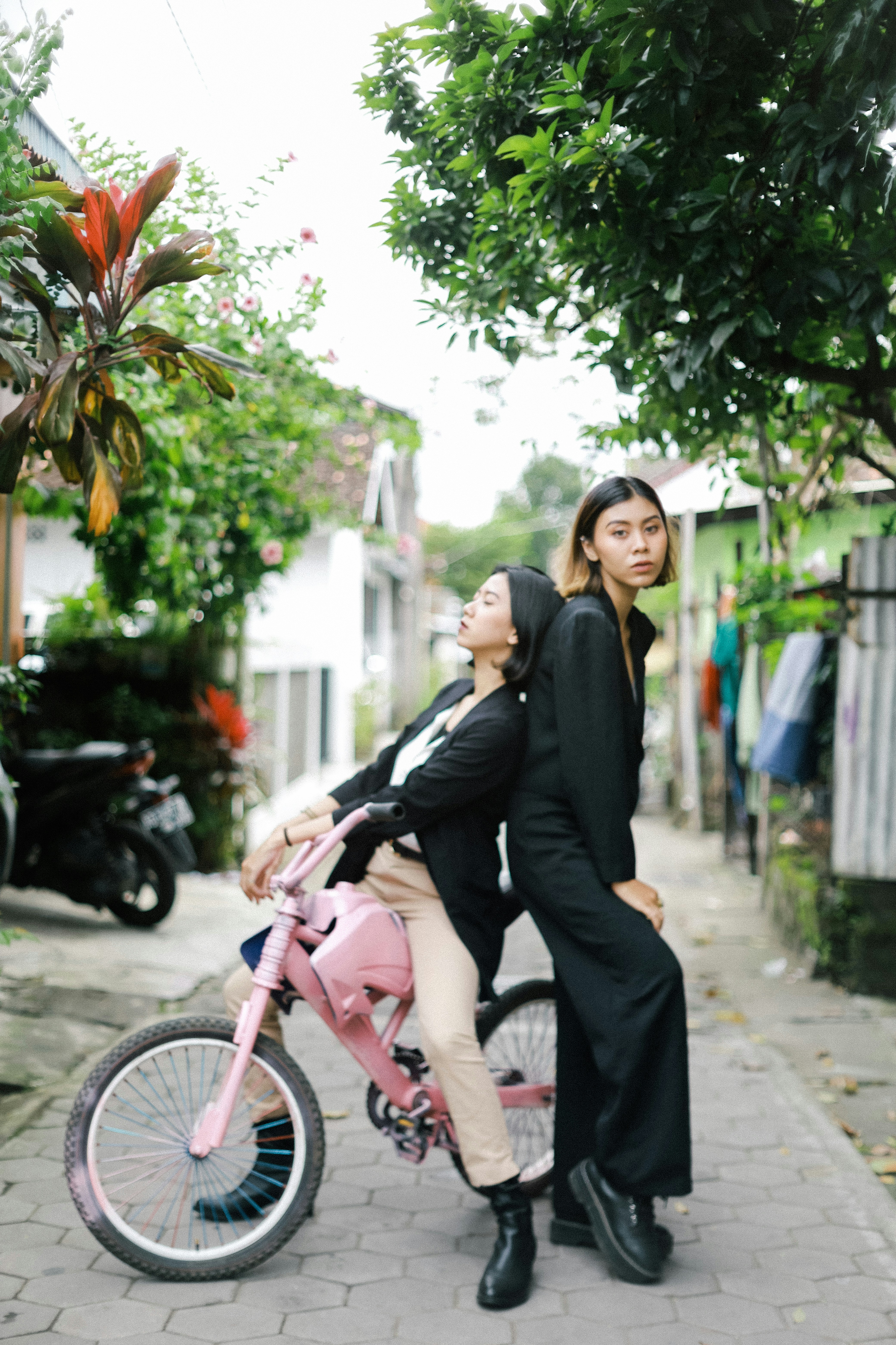 Wanita dengan blazer hitam dan celana hitam duduk di atas sepeda merah muda di siang hari