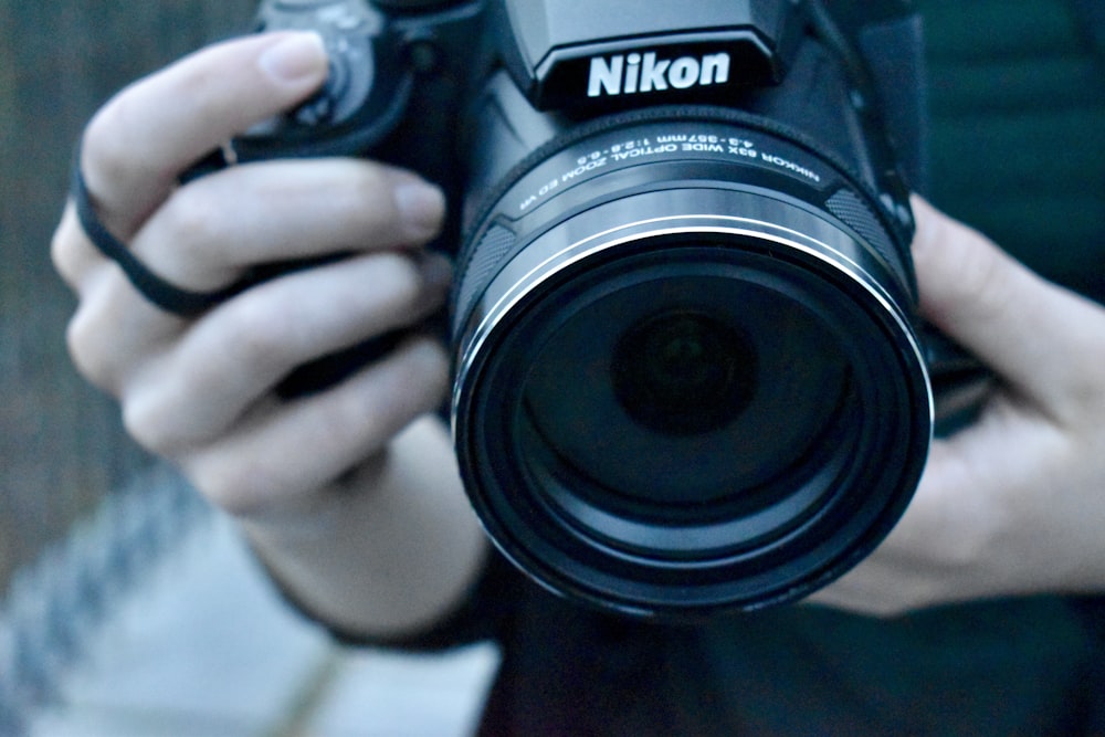 Person mit schwarzer Nikon DSLR-Kamera
