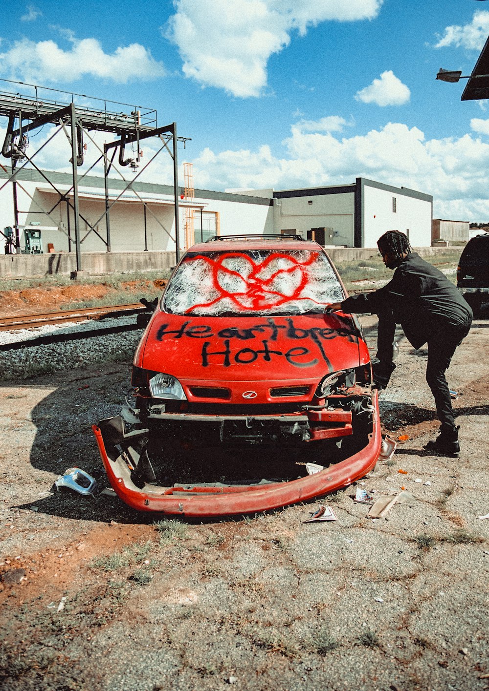 man in black jacket standing beside red car