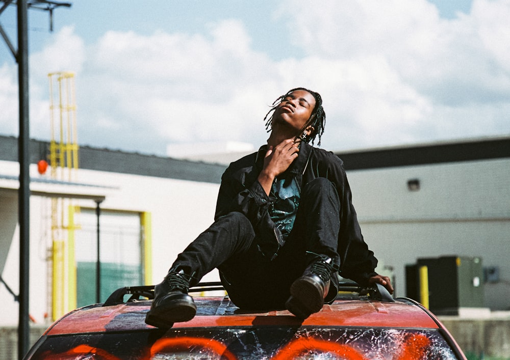 woman in black leather jacket sitting on red car hood during daytime