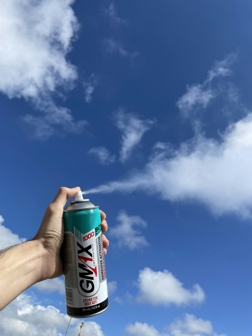 Persona che tiene la bomboletta spray verde e bianca sotto il cielo blu e le nuvole bianche durante il giorno