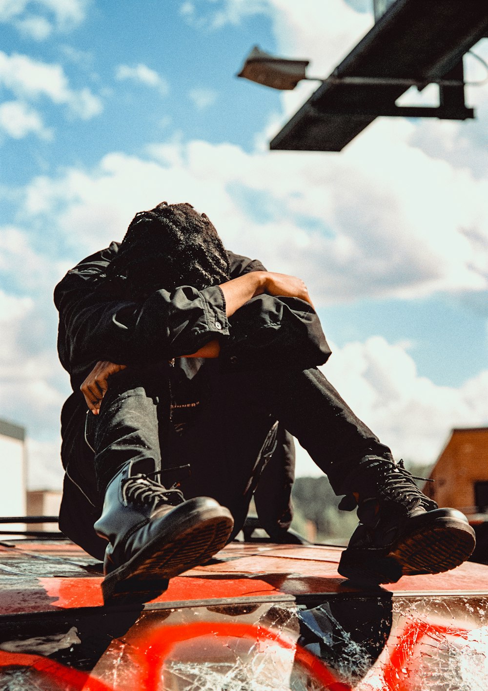 man in black jacket and black pants sitting on brown wooden bench under white clouds and