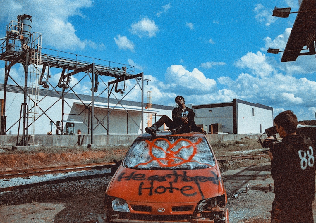 man in black jacket sitting on orange car hood during daytime