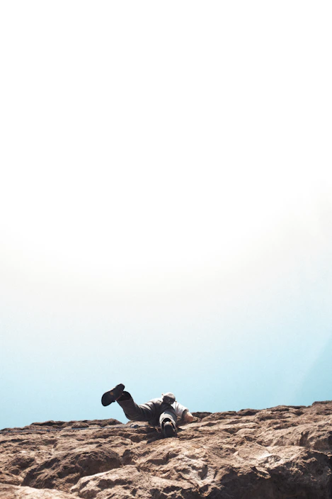 A climber gripping a rugged rock face under a bright blue sky, embodying adventure and focus.