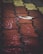 Raindrops create small splashes on patterned paving stones, with a solitary brown leaf resting on the wet surface. The paving consists of interlocking bricks in shades of red, yellow, and brown, reflecting the dampness.