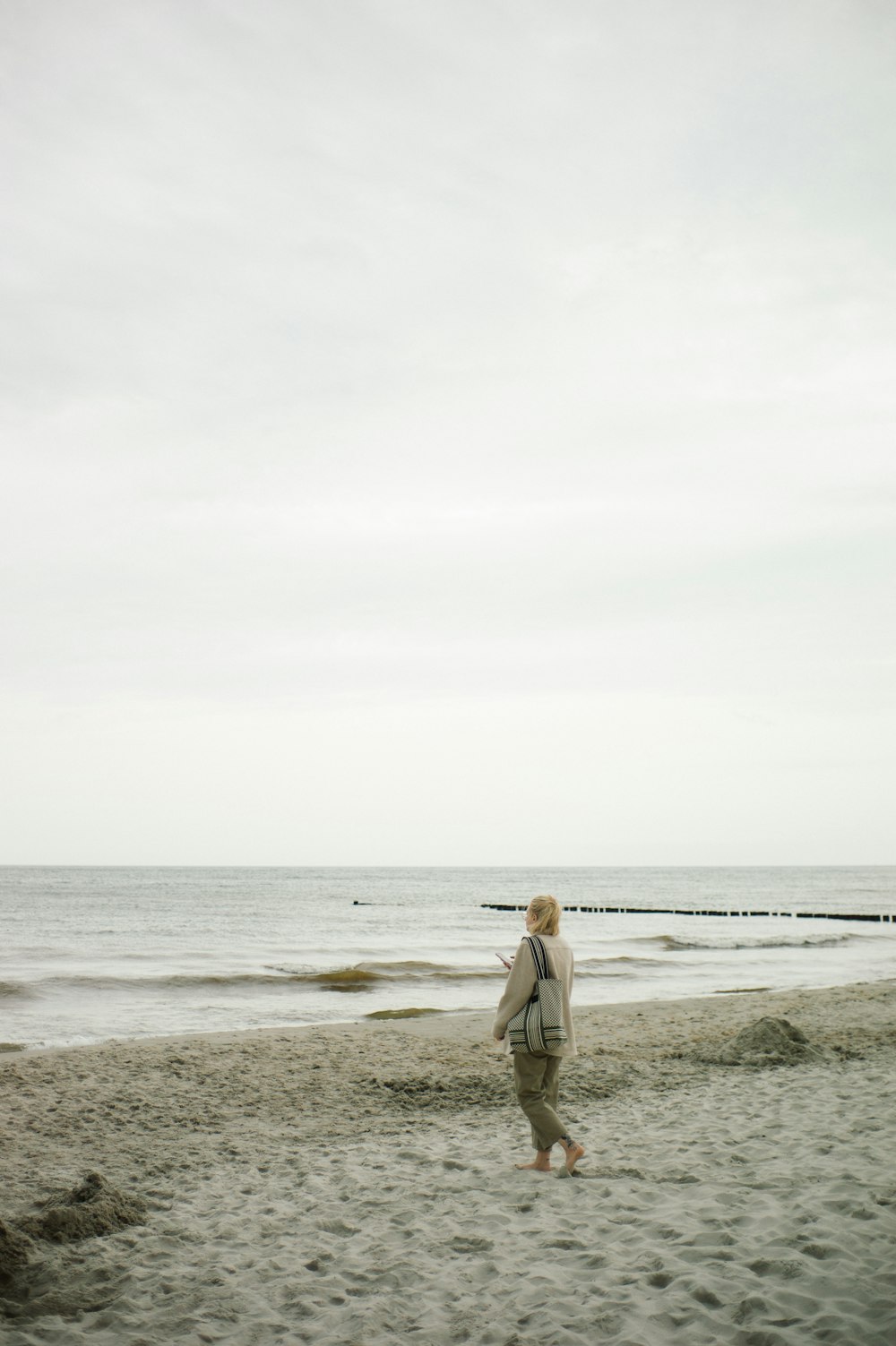 낮 동안 해변을 걷고 있는 갈색 코트를 입은 여자