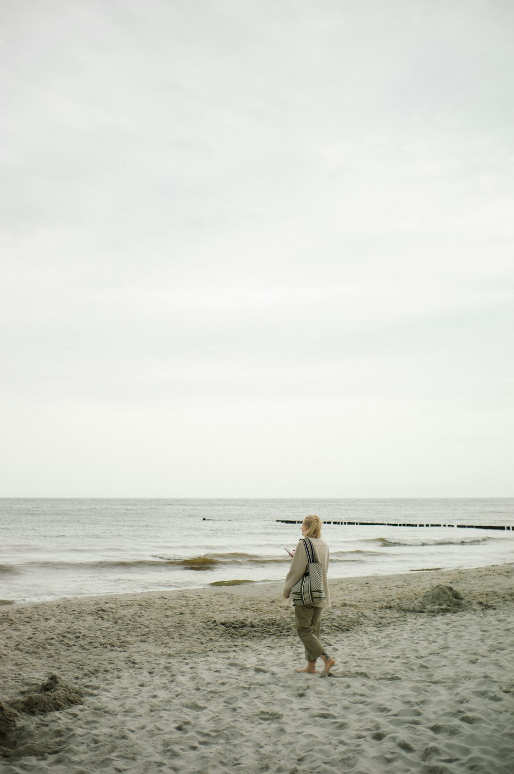 woman in brown coat walking on beach during daytime