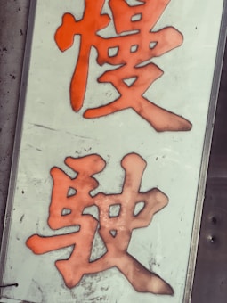 Large orange Chinese characters are displayed on a white vertical rectangular sign against a metal background. The characters appear bold and stylized.