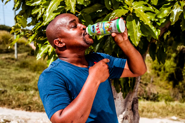 A happy customer holding a zesti drinks bottle outdoors with soft green leaves in the background.