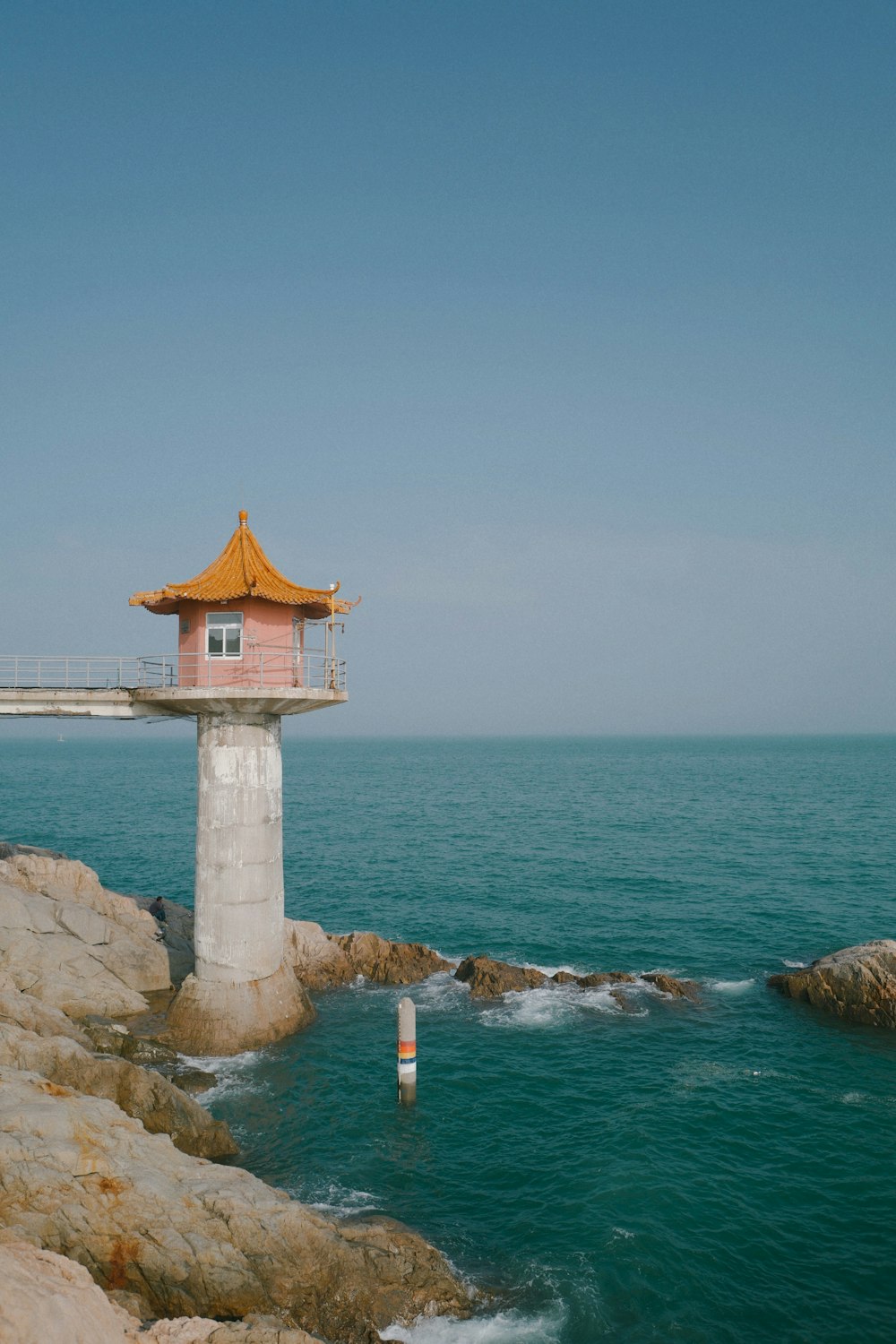 white and orange concrete tower on brown rock formation near body of water during daytime