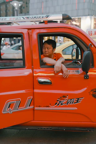 Close-up of a confident driver checking delivery documents beside a bright orange-accented truck.