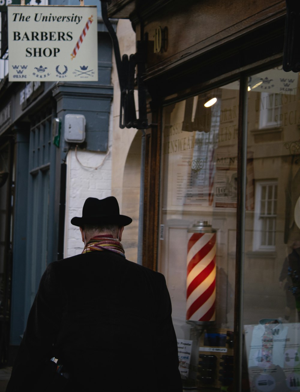 man in black suit jacket wearing black hat standing near store during daytime