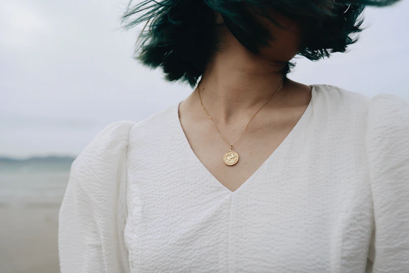 Adult woman in a white linen top wearing a small gold pendant by the sea