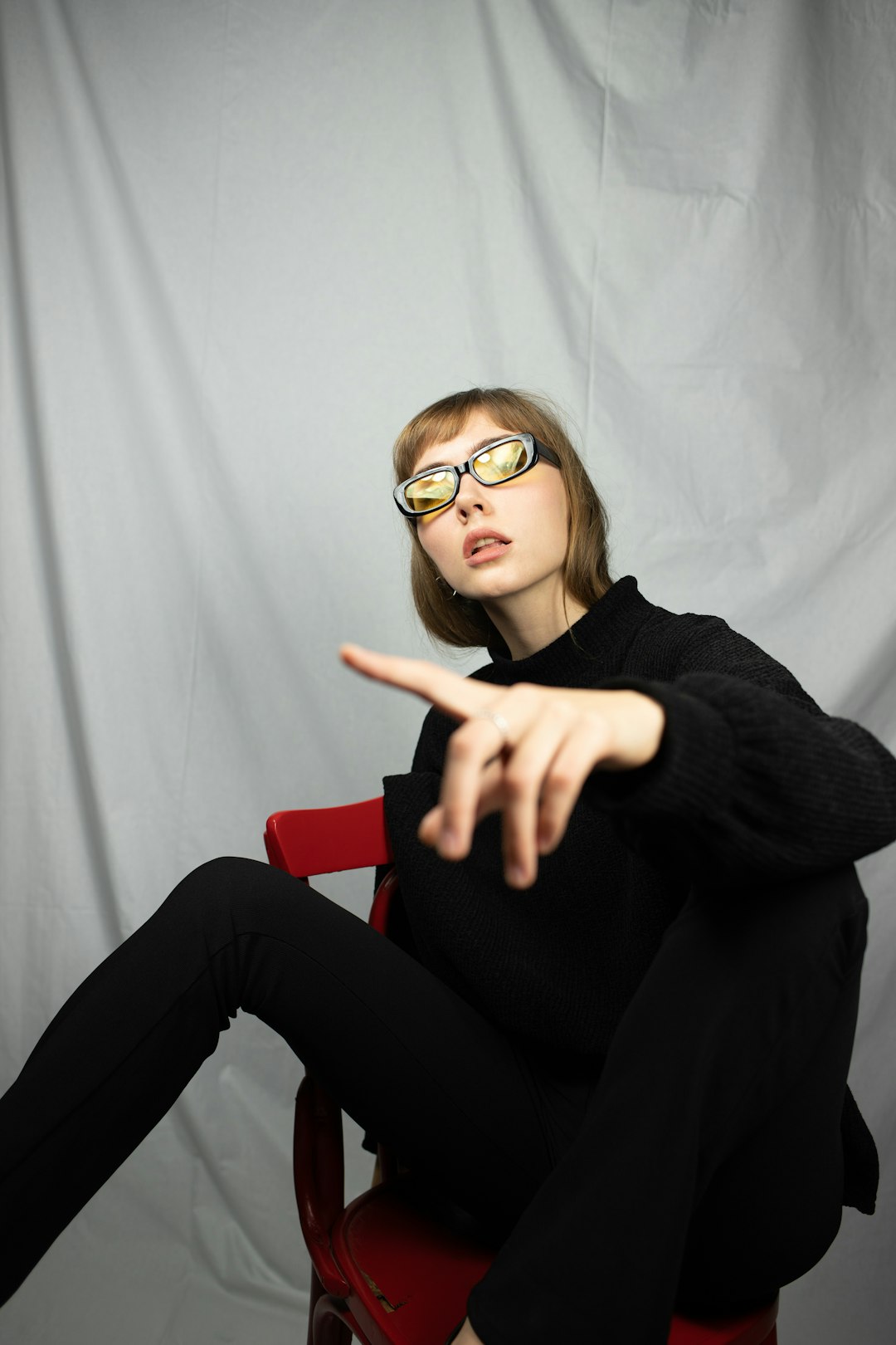 woman in black sweater and black pants wearing eyeglasses sitting on red chair