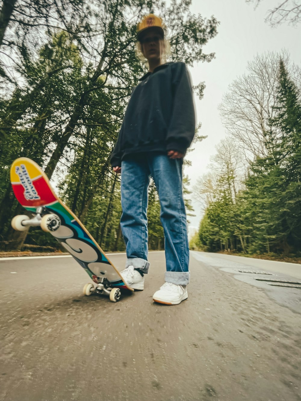 man in black jacket and blue denim jeans holding skateboard