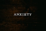 A dark wooden textured background with the word 'ANXIETY' in white capital letters centered prominently.