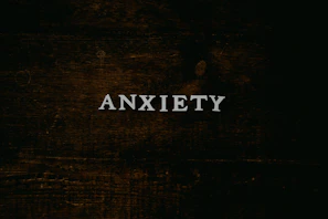 A dark wooden textured background with the word 'ANXIETY' in white capital letters centered prominently.