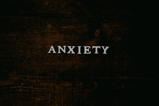 A dark wooden textured background with the word 'ANXIETY' in white capital letters centered prominently.
