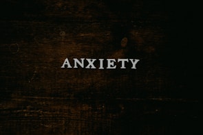A dark wooden textured background with the word 'ANXIETY' in white capital letters centered prominently.