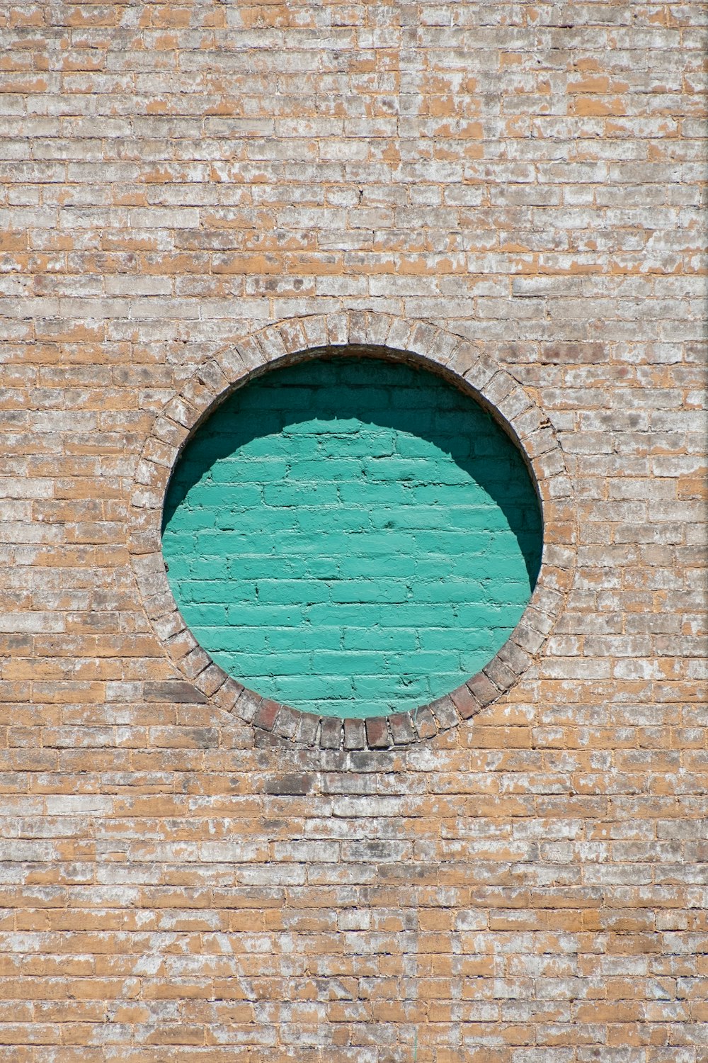 muro di mattoni marroni con finestra di vetro rotonda blu