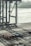 A large industrial shipping port with cranes towering over a wide area. Multiple cargo containers are neatly arranged on the ground, with some labeled with brand names. The background includes a body of water with large ships, contributing to a busy and industrious atmosphere.