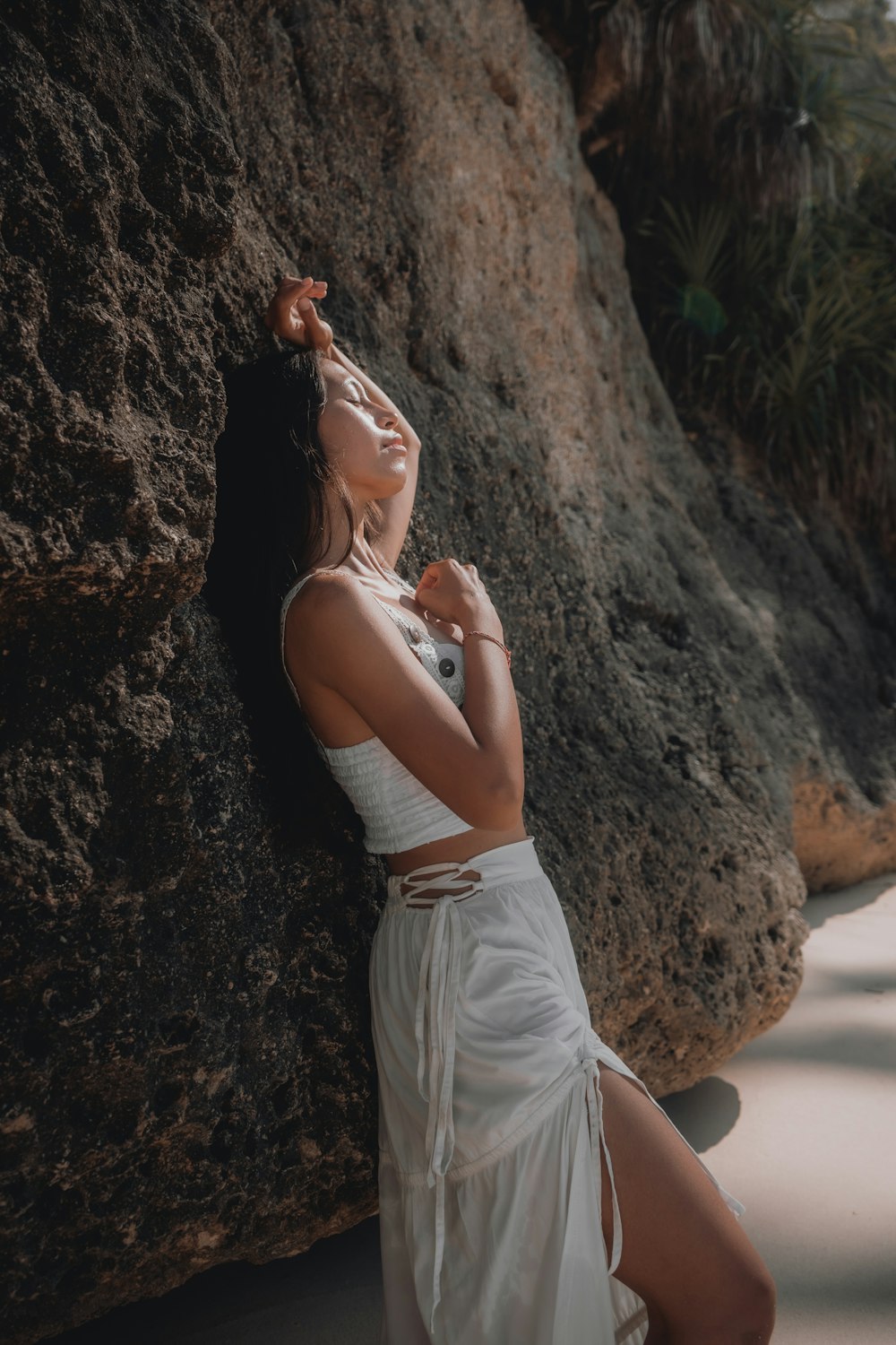 woman in white tank top and white shorts leaning on brown rock