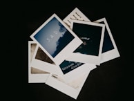 A stack of Polaroid photos on a dark background. The top photo features the word 'S.A.D' against a silhouette of trees. Other photos display words like 'lonely' and 'seasonal affective disorder' in a handwritten style.