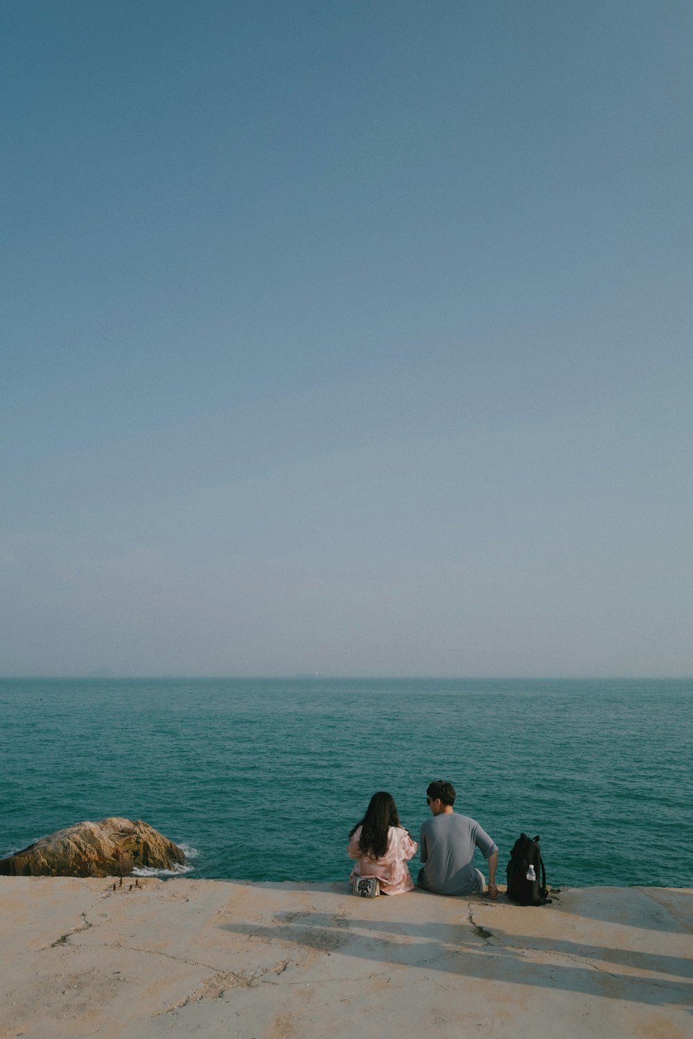 man and woman sitting on rock formation near sea during daytime