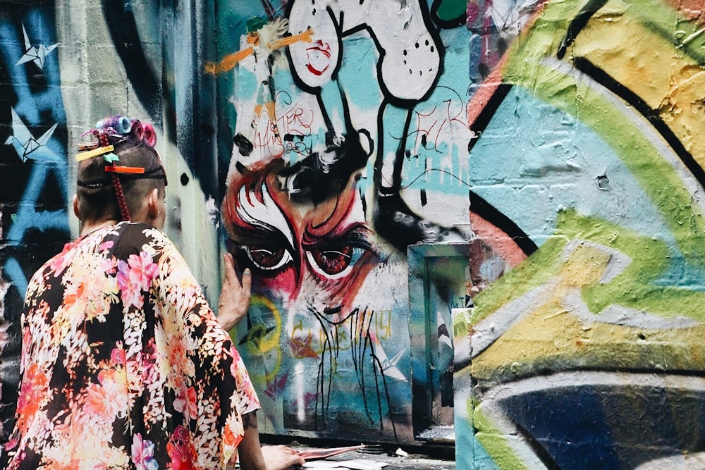 Frau in rot-weißem Blumenkleid, die tagsüber an der Graffiti-Wand steht