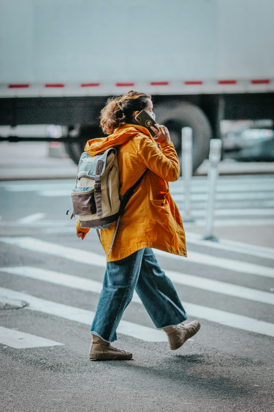 woman in brown coat and blue denim jeans standing on pedestrian lane during daytime