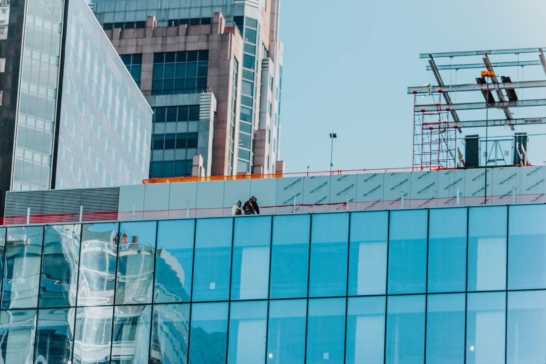 man in black jacket and black pants standing on glass building during daytime