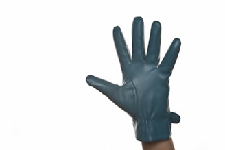 A teal leather glove is worn on a hand, with fingers spread out against a plain white background. The glove material looks smooth and shiny, highlighting the texture and form-fitting design.