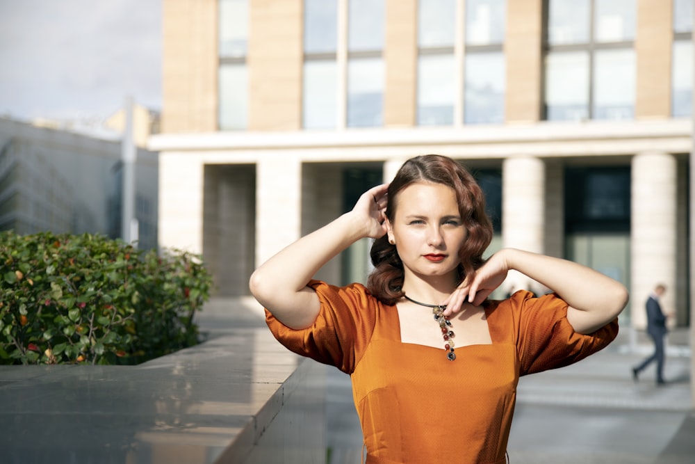 woman in orange long sleeve shirt standing on sidewalk during daytime