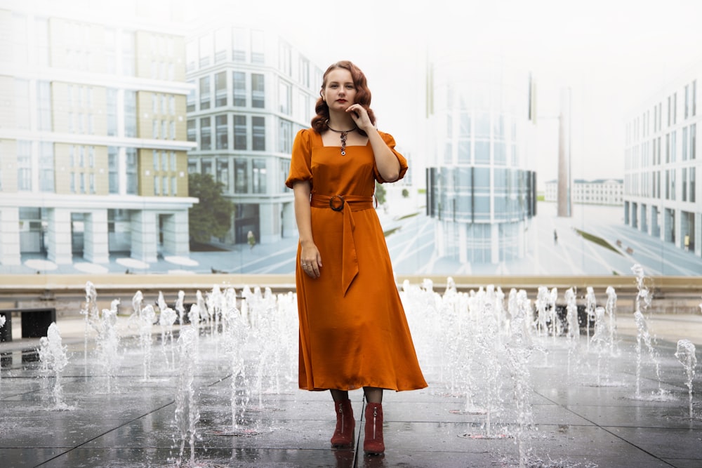 woman in orange dress standing on water fountain during daytime
