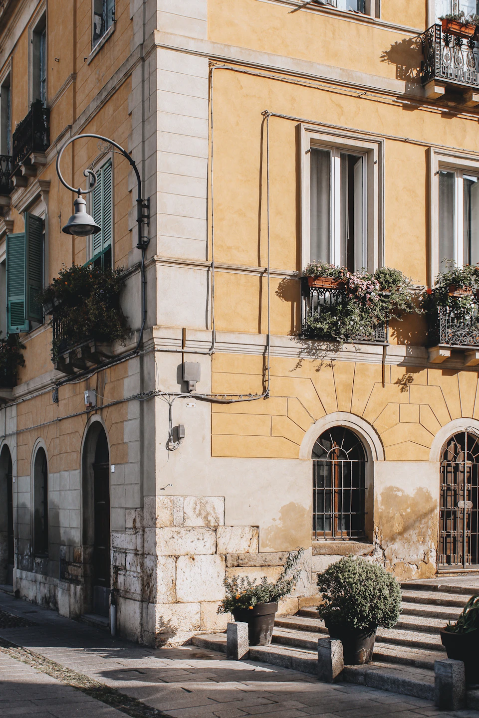 Yellow building with curved corner and potted plants on balcony in stone facade setting