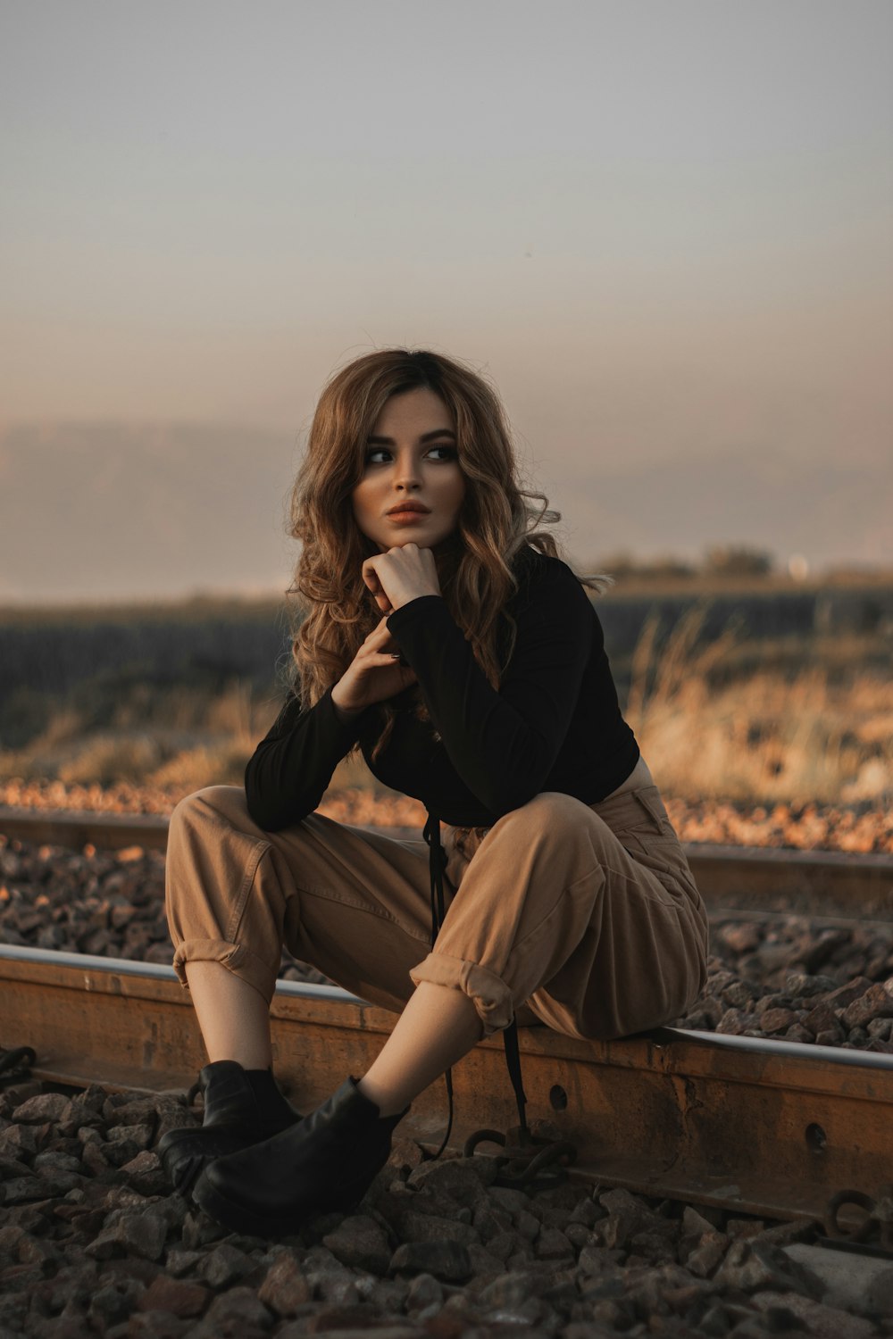 mulher na camisa preta de manga comprida e calças marrons sentadas no banco de madeira marrom durante o dia