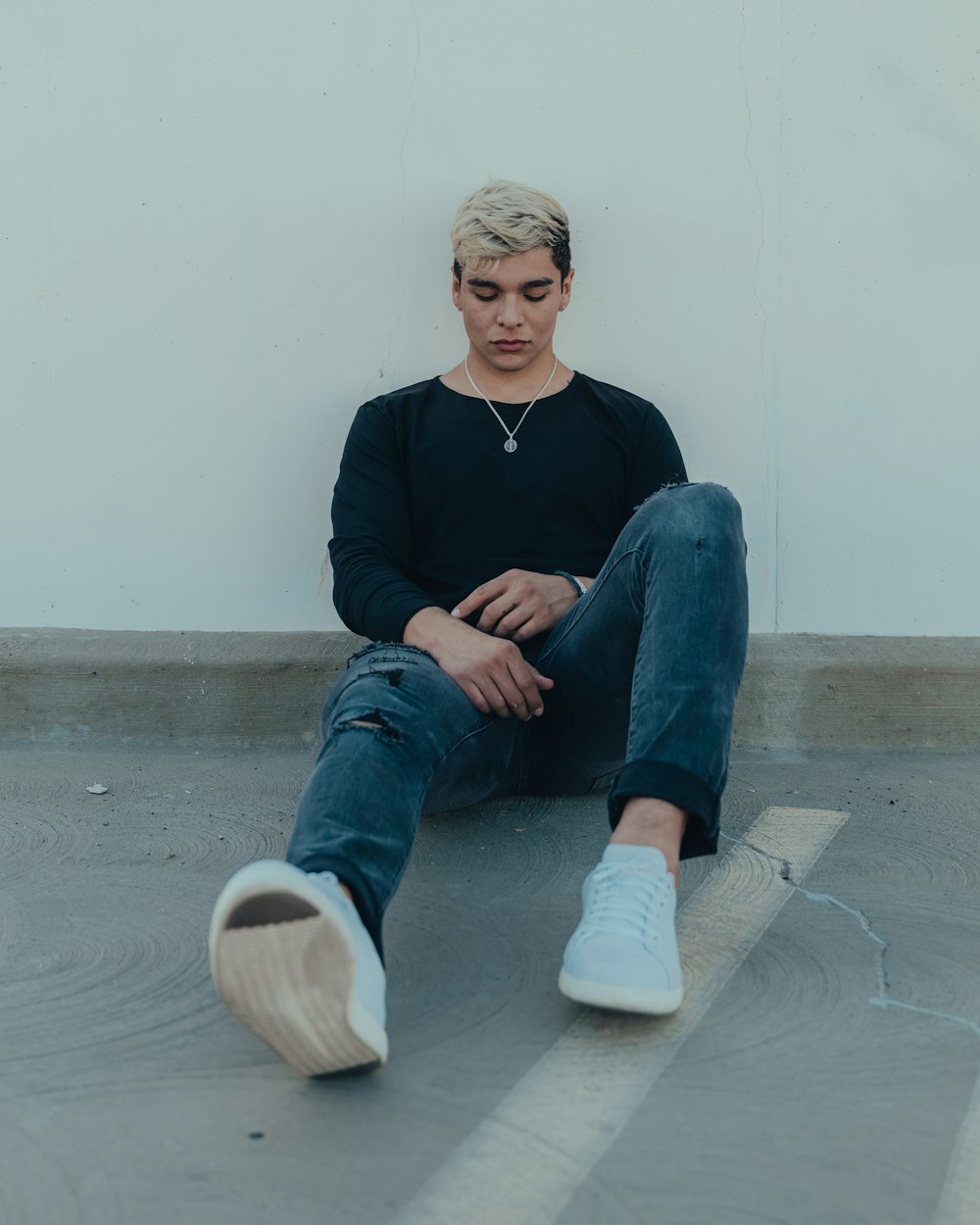 man in black v neck sweater and blue denim jeans sitting on concrete floor