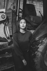A black and white photo featuring a person standing confidently beside a large vehicle tire. The setting suggests an industrial or rural environment.