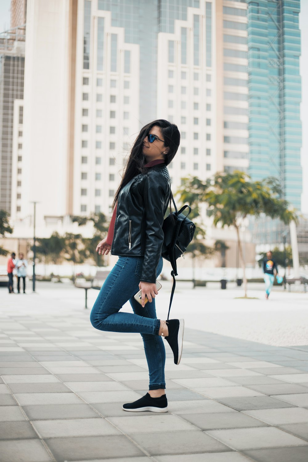 Frau in schwarzer Jacke und blauen Jeans tagsüber auf dem Bürgersteig