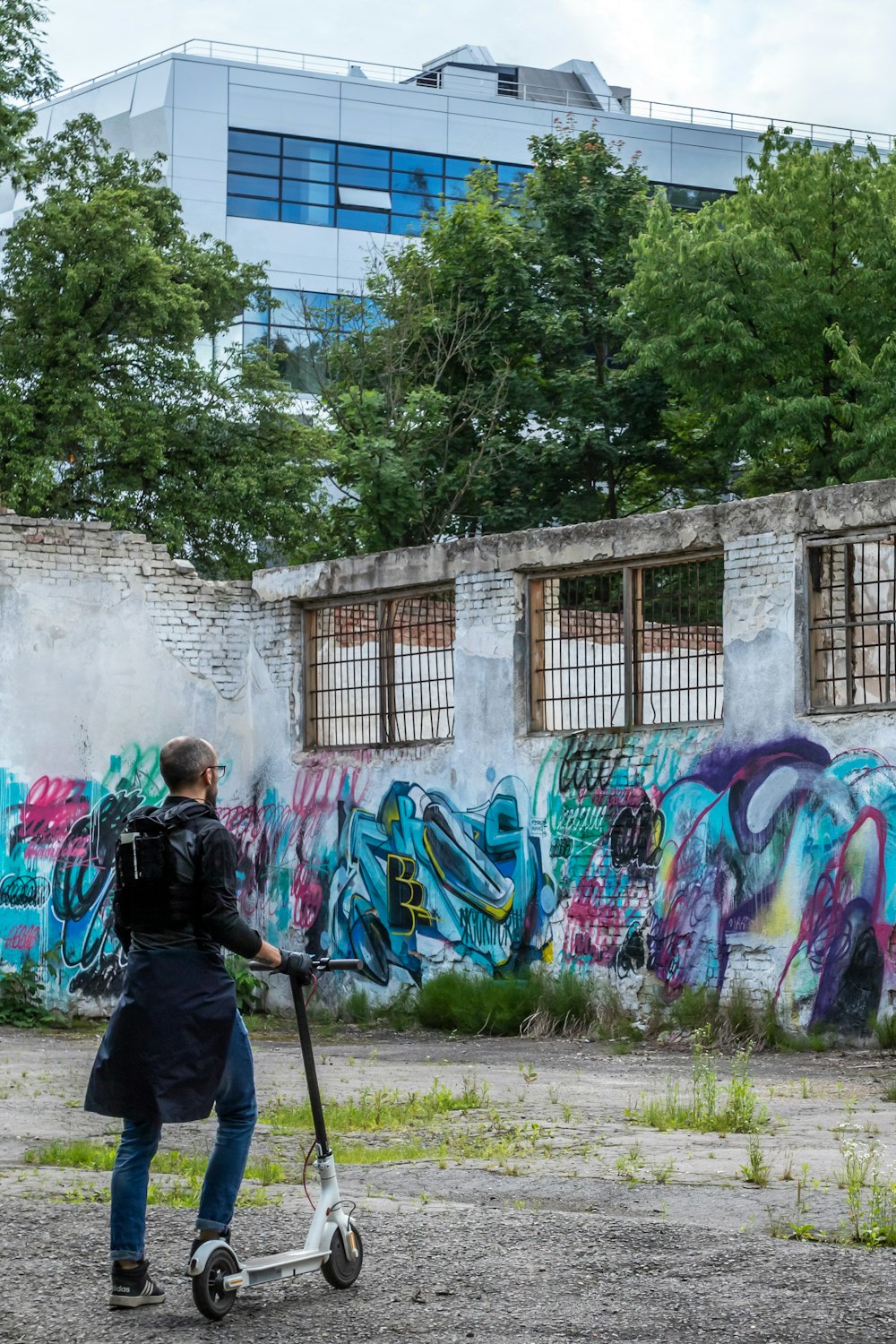 mulher na jaqueta preta andando na estrada de terra perto da parede do grafite durante o dia