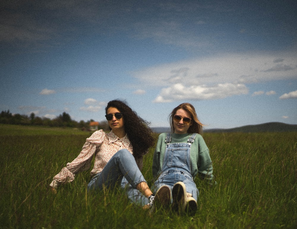 2 women sitting on green grass field under blue sky during daytime