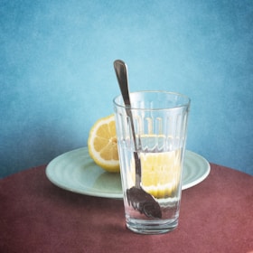 Glass of water with lemon and fresh vegetables on a kitchen counter.