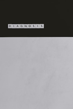 A series of Scrabble tiles spelling out the word 'DIAGNOSIS' is arranged horizontally on a surface. The background is divided, with a dark upper section and a light lower section.