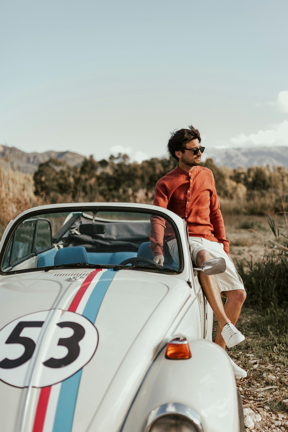 man in red jacket standing beside white coupe during daytime