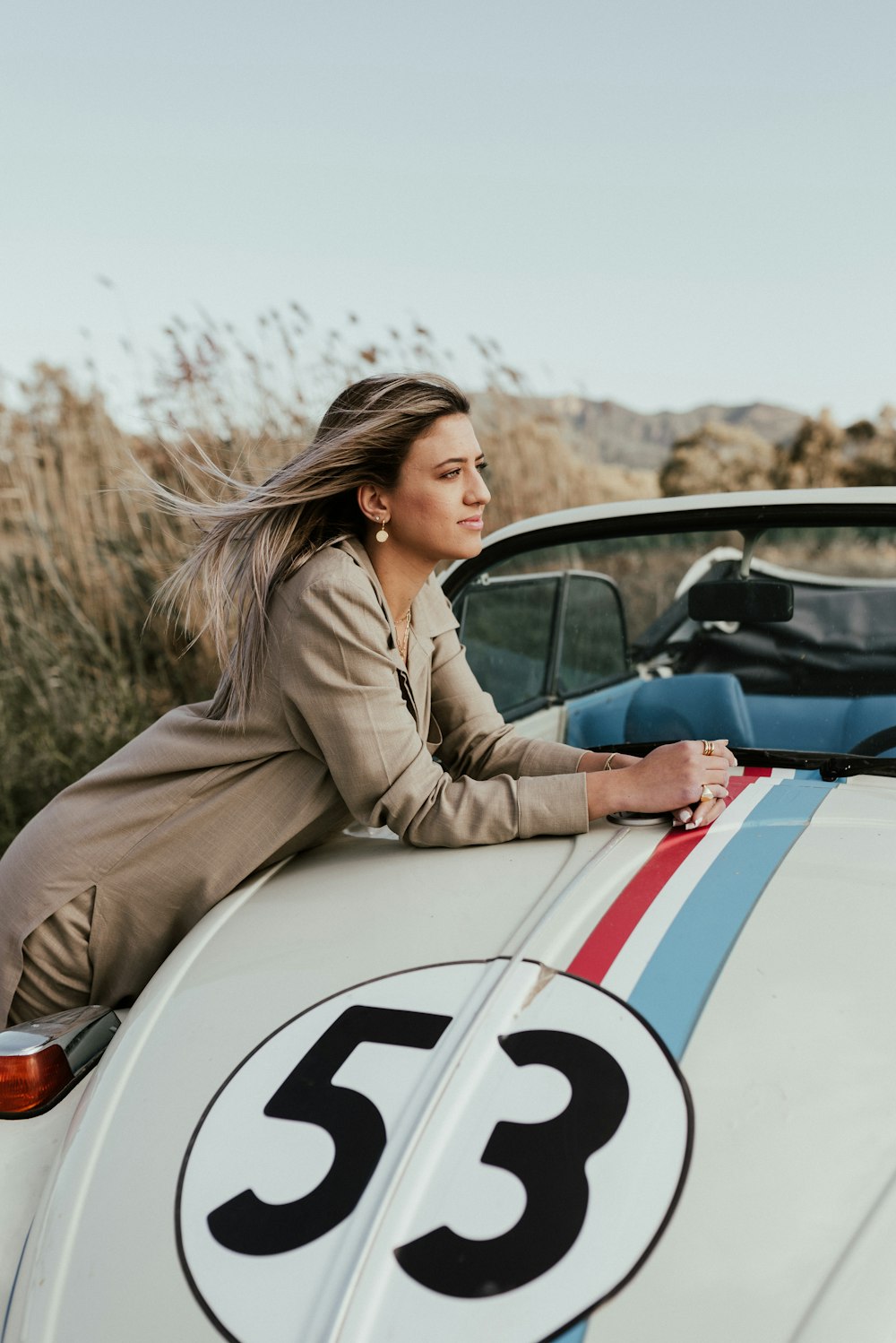 woman in brown coat sitting on white and blue car during daytime