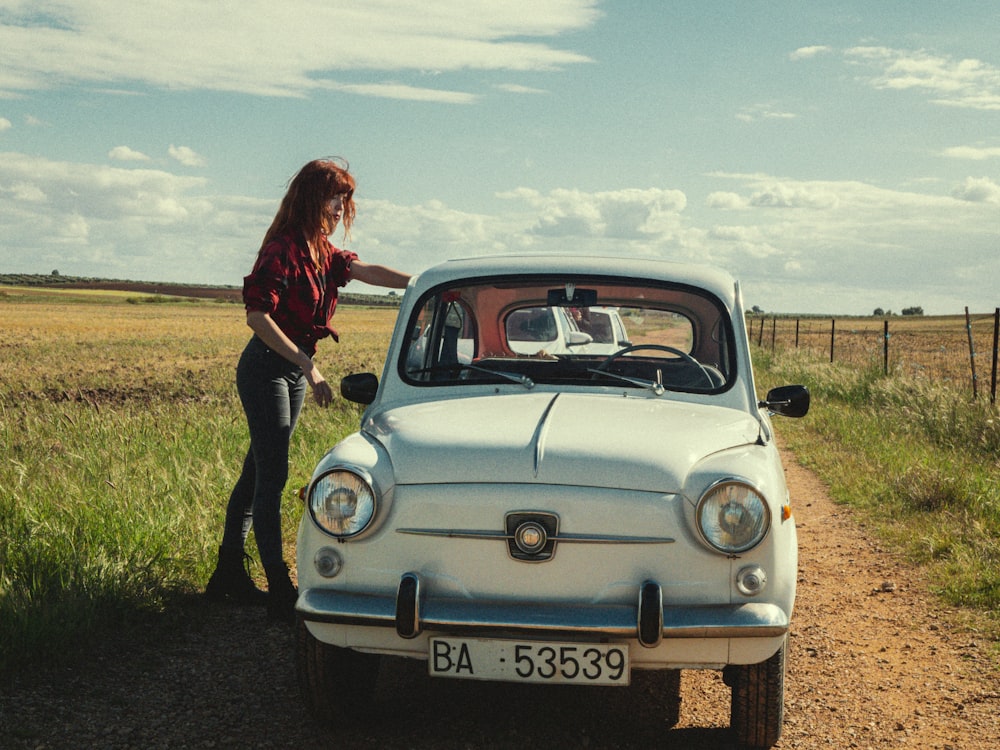 man in red jacket standing beside blue volkswagen beetle