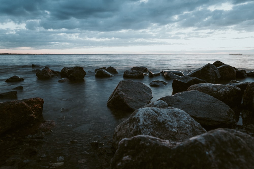 gray and black rocks on sea shore under cloudy sky during daytime